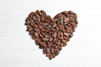Heart made of cocoa beans on white wooden table, top view