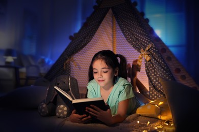 Photo of Little girl reading fairy tale in play tent at home
