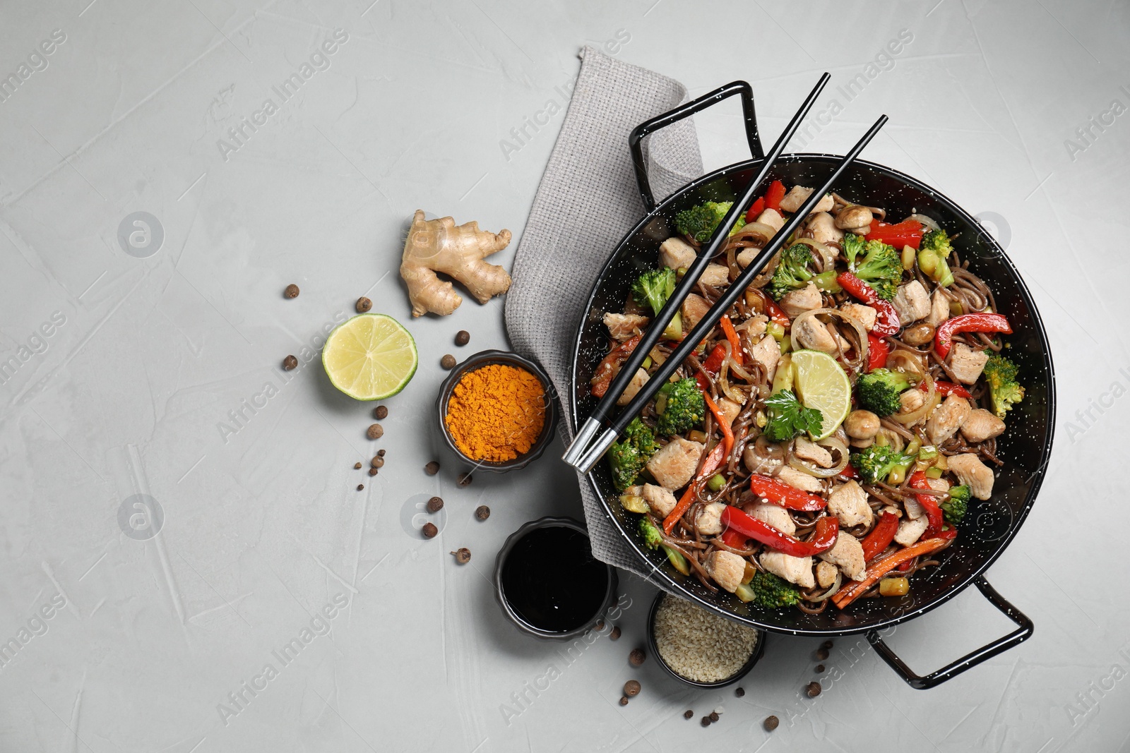 Photo of Stir-fry. Tasty noodles with meat in wok, chopsticks and ingredients on grey textured table, flat lay. Space for text