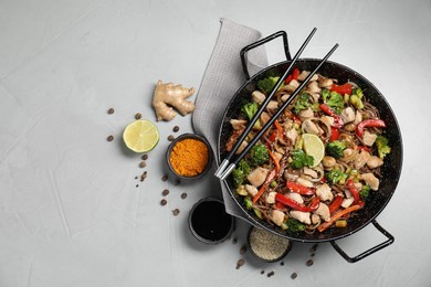 Stir-fry. Tasty noodles with meat in wok, chopsticks and ingredients on grey textured table, flat lay. Space for text