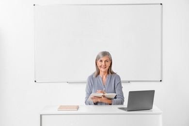 Photo of Happy professor giving lecture near laptop at desk in classroom, space for text