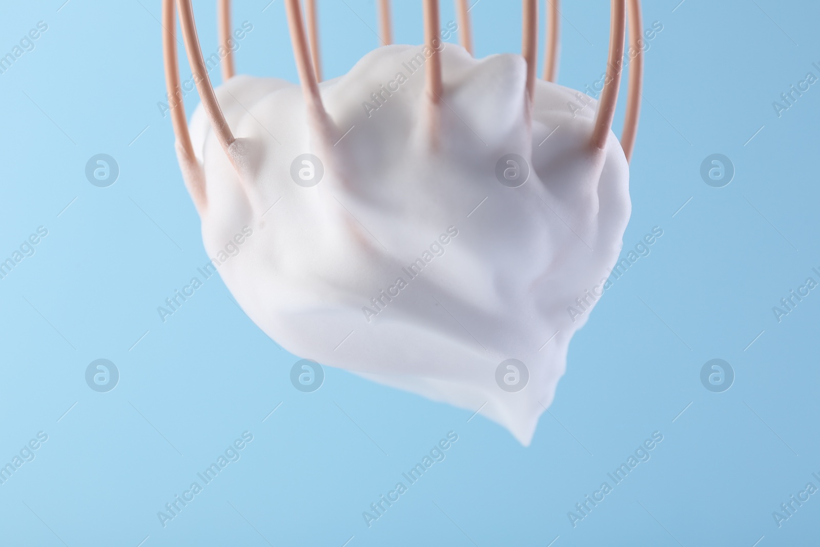 Photo of Whisk with whipped cream on light blue background, closeup