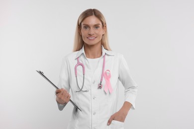 Doctor with pink ribbon, clipboard and stethoscope on white background. Breast cancer awareness