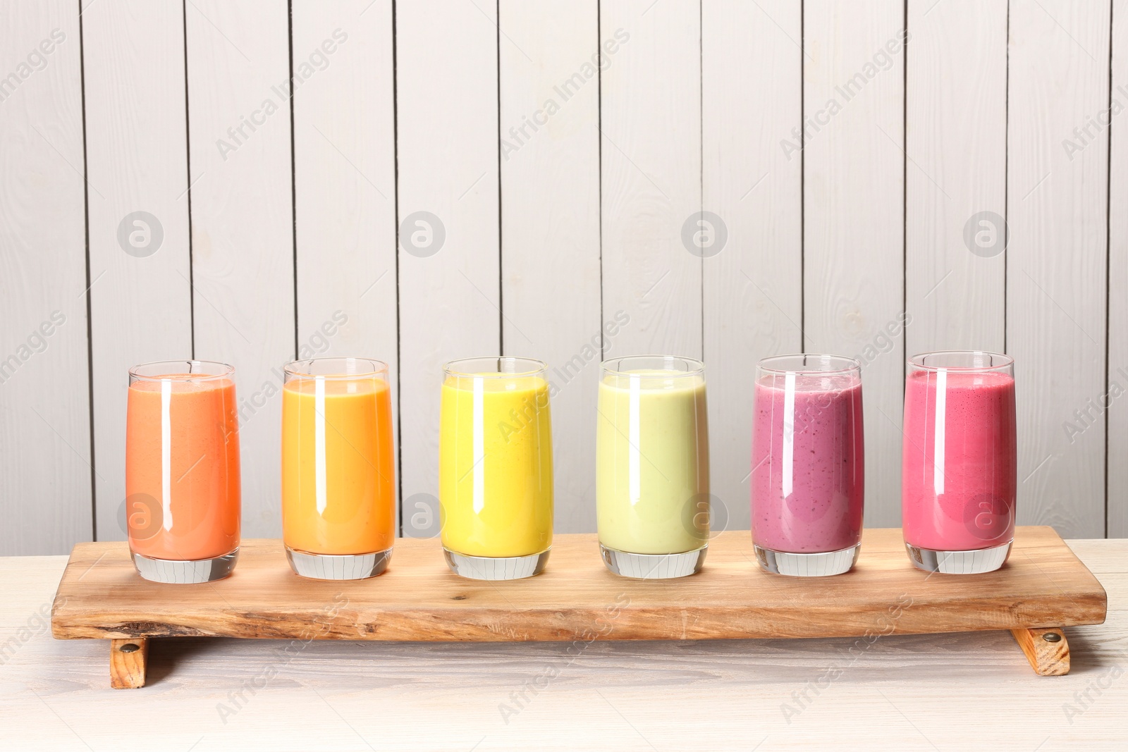 Photo of Board with many different tasty smoothies against white wooden background, space for text