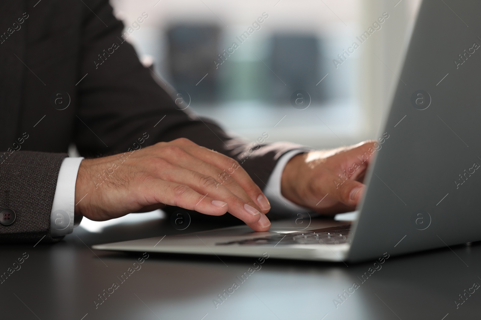 Photo of Man using modern laptop at black desk in office, closeup