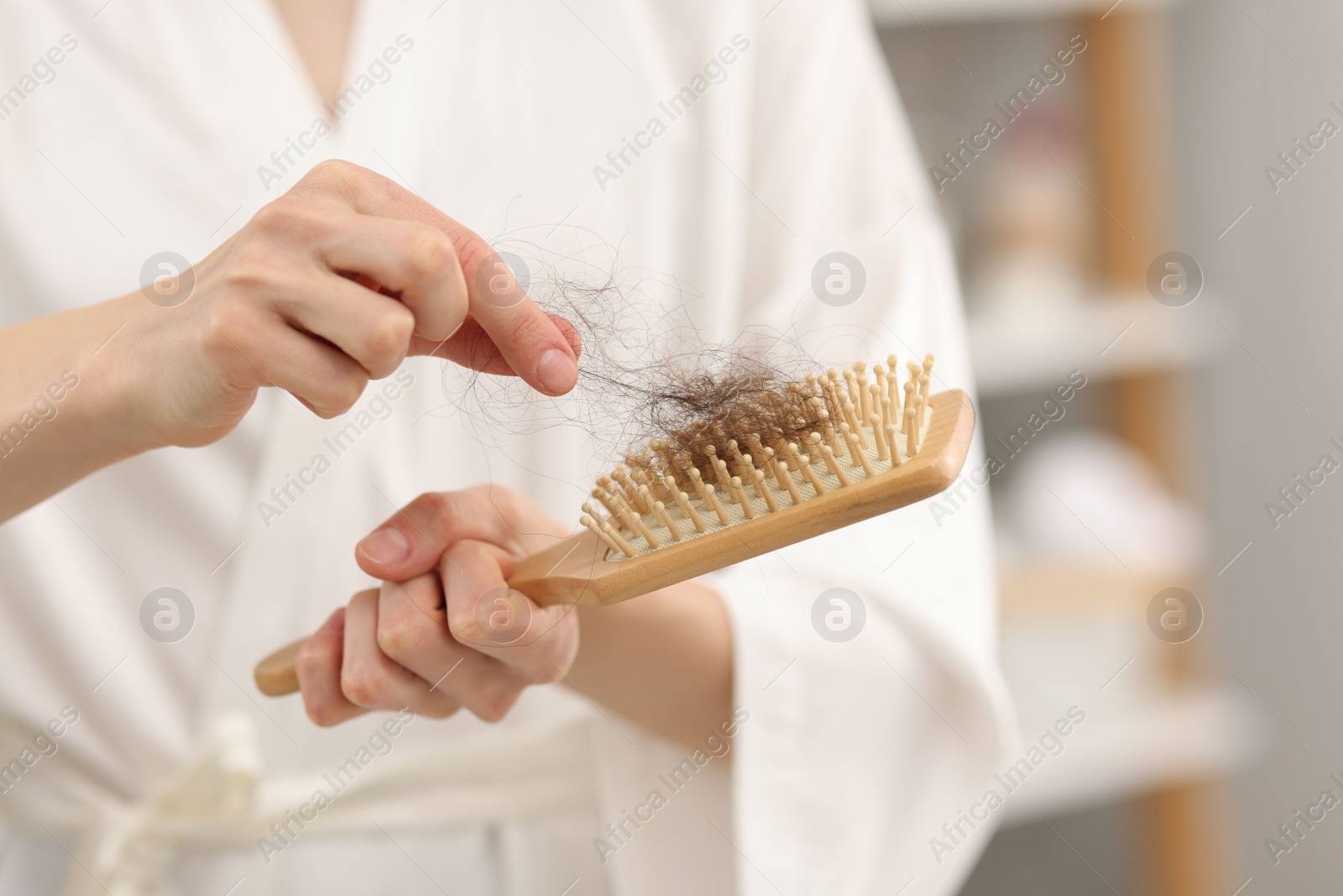 Photo of Woman taking her lost hair from brush at home, closeup. Alopecia problem