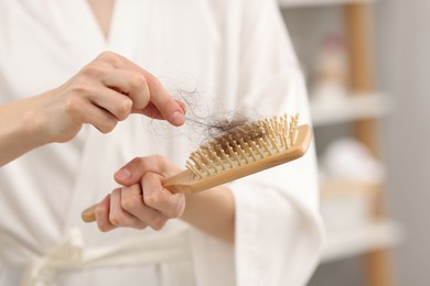 Photo of Woman taking her lost hair from brush at home, closeup. Alopecia problem