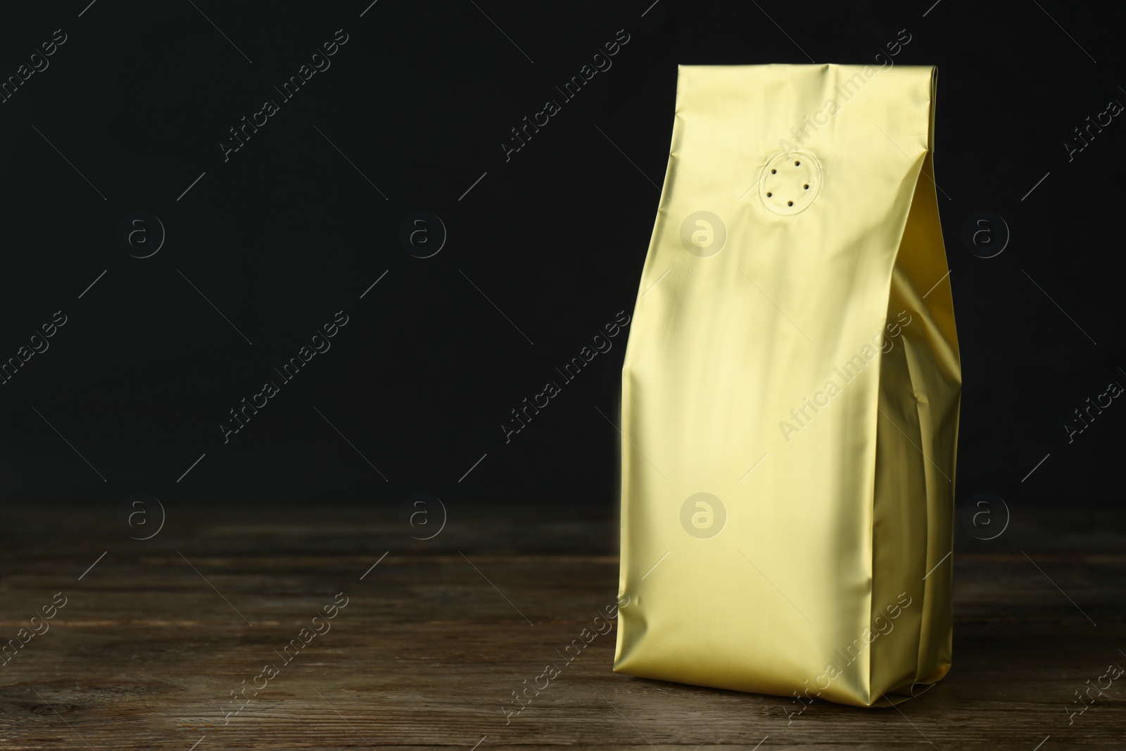 Photo of One blank foil package on wooden table against dark background. Space for text