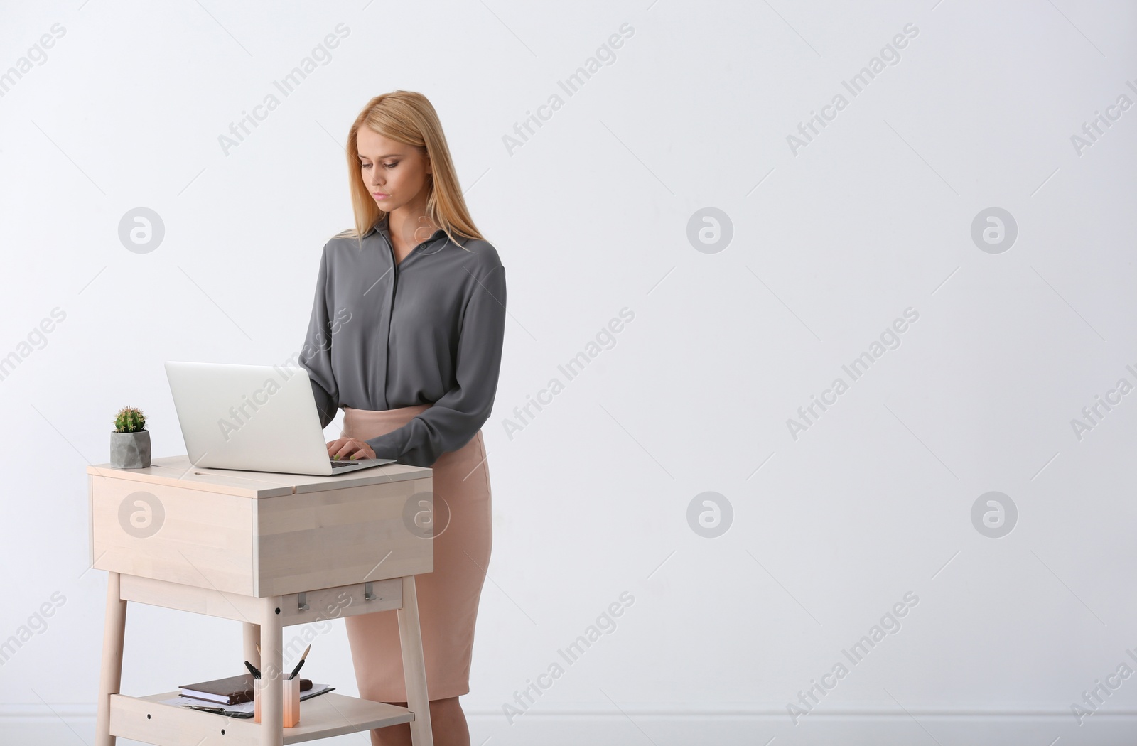 Photo of Young woman using laptop at stand up workplace against white wall. Space for text