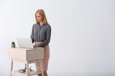 Young woman using laptop at stand up workplace against white wall. Space for text