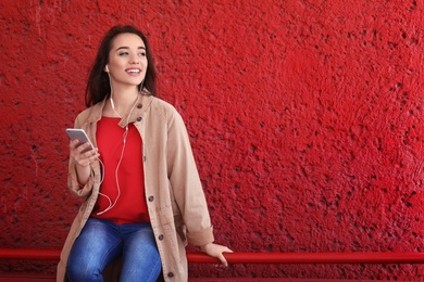 Young woman using phone for listening to music on color background