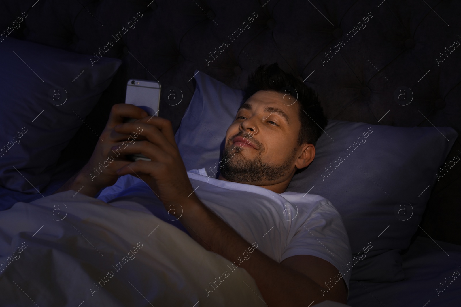 Photo of Handsome man using smartphone at night. Bedtime