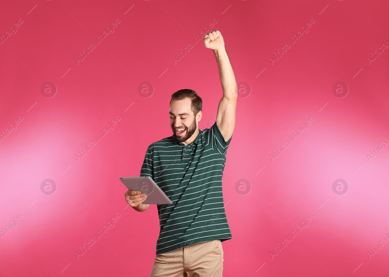 Photo of Emotional young man with tablet celebrating victory on color background