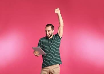 Photo of Emotional young man with tablet celebrating victory on color background