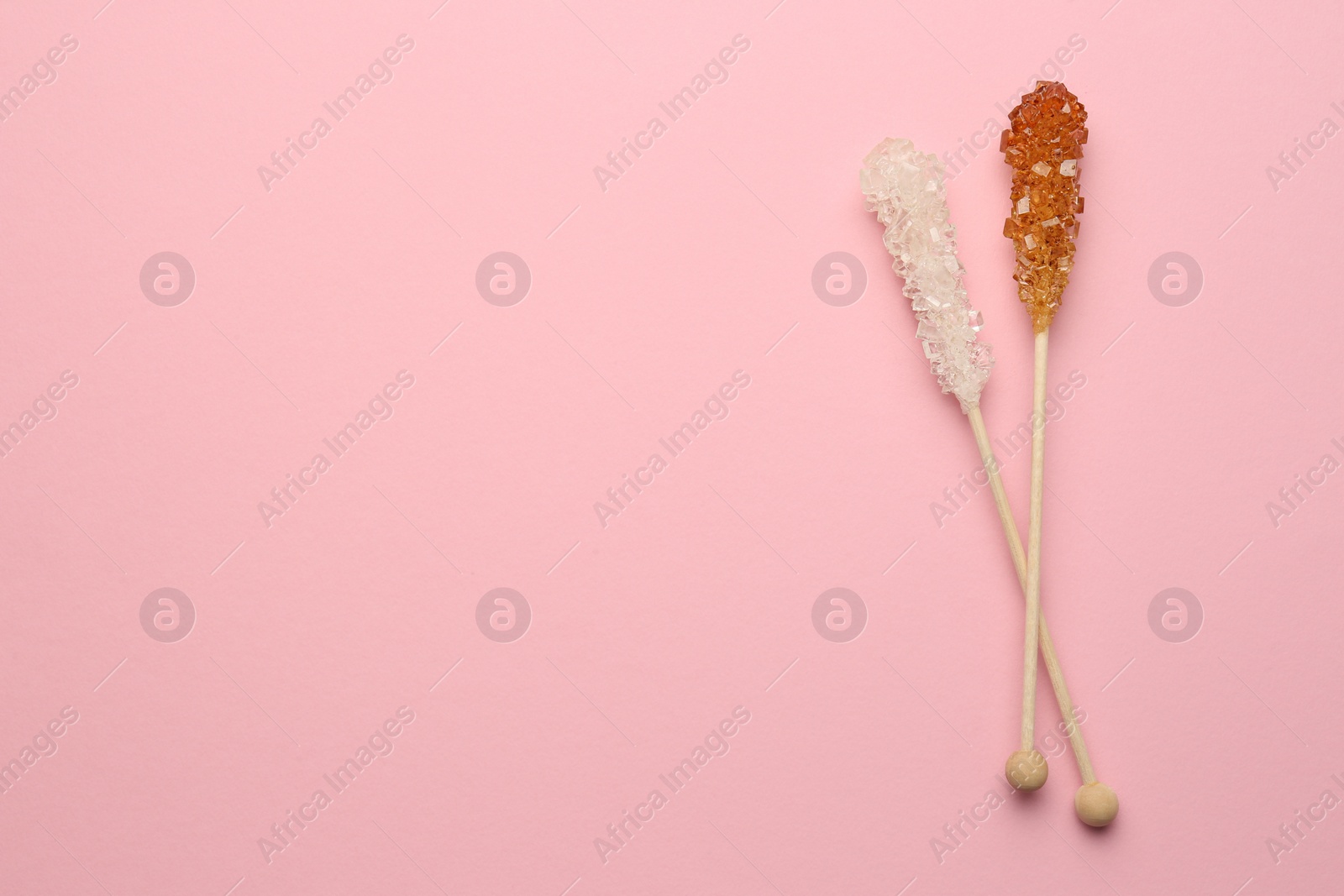 Photo of Wooden sticks with sugar crystals and space for text on pink background, flat lay. Tasty rock candies