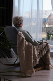 Photo of Elderly woman sitting in rocking chair indoors, back view. Loneliness concept