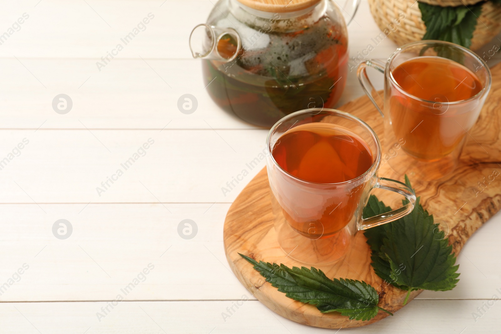 Photo of Aromatic nettle tea and green leaves on white wooden table, space for text