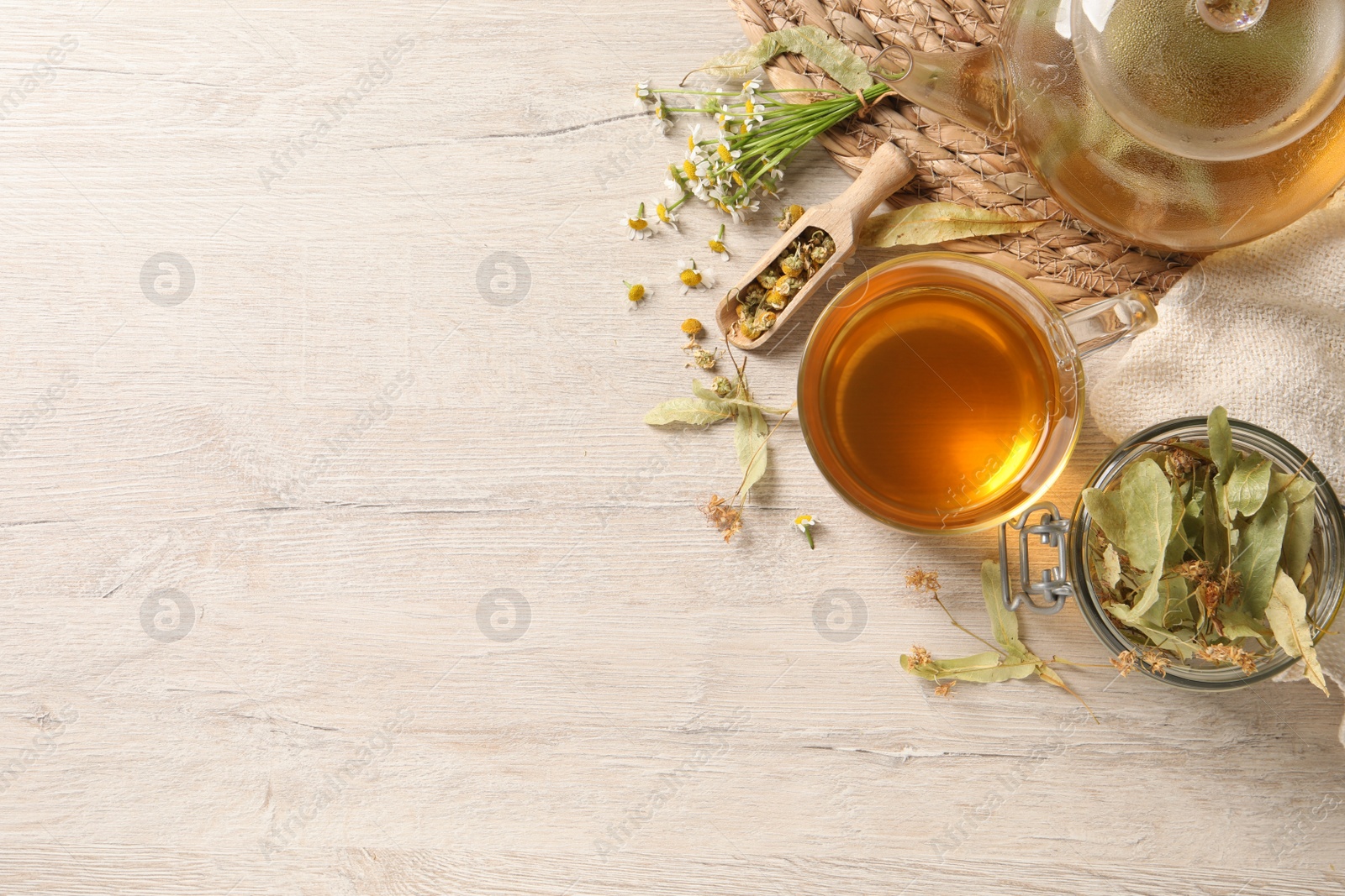 Photo of Freshly brewed tea and dried herbs on white wooden table, flat lay. Space for text