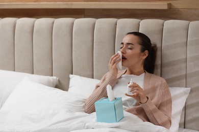 Photo of Sick young woman with napkins and nasal spray in bed at home
