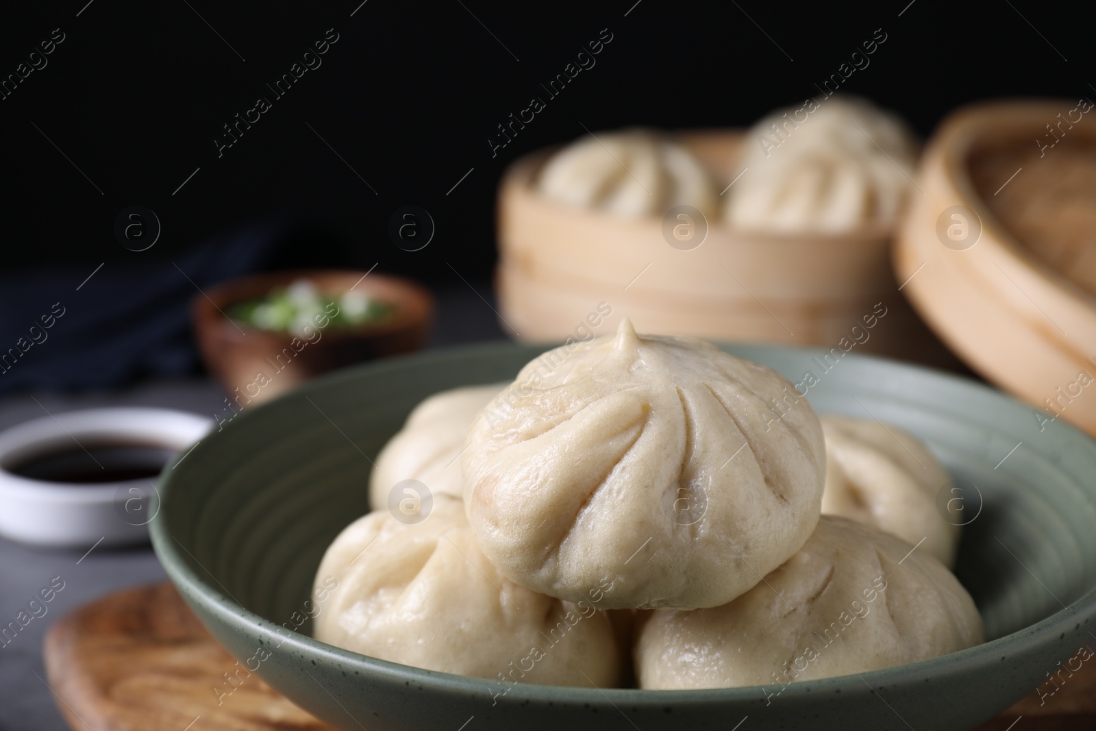 Photo of Delicious bao buns (baozi) in bowl on grey table, closeup