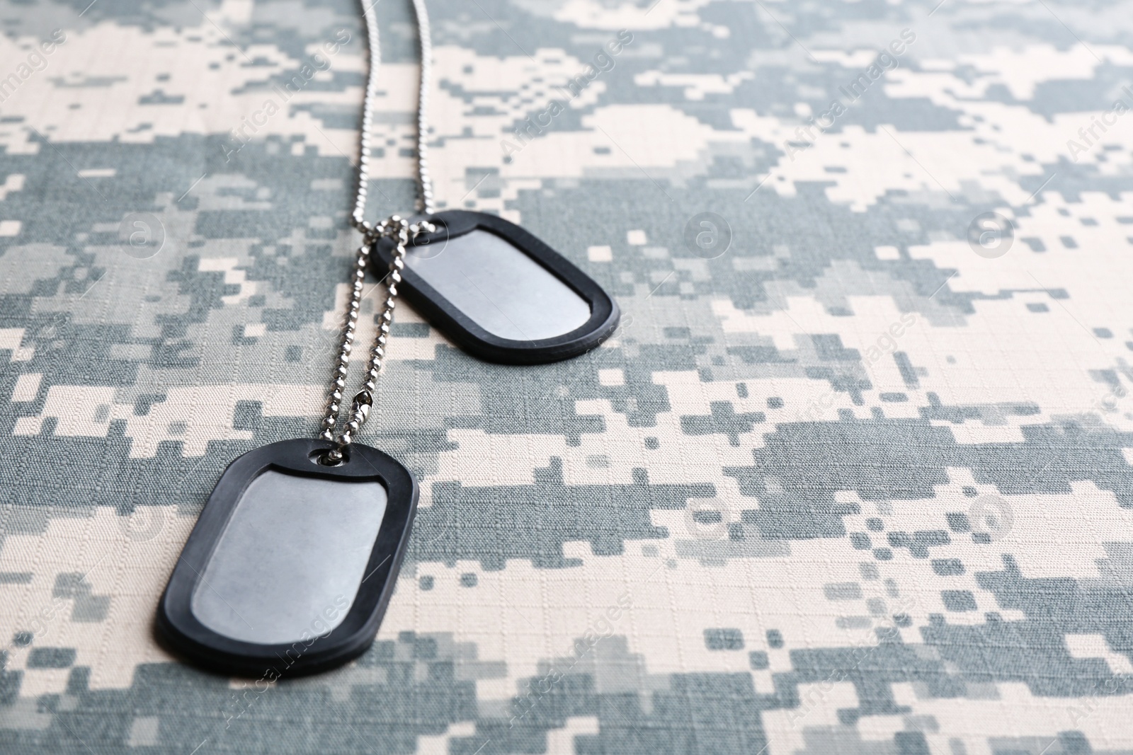 Photo of Metal military ID tags on camouflage background. Space for text