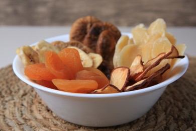 Bowl with different dried fruits on wicker mat, closeup