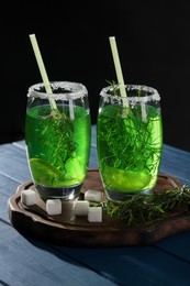 Photo of Glasses of homemade refreshing tarragon drink, sprigs and sugar cubes on blue wooden table
