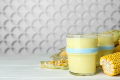 Photo of Fresh corn milk and cobs on white wooden table. Space for text