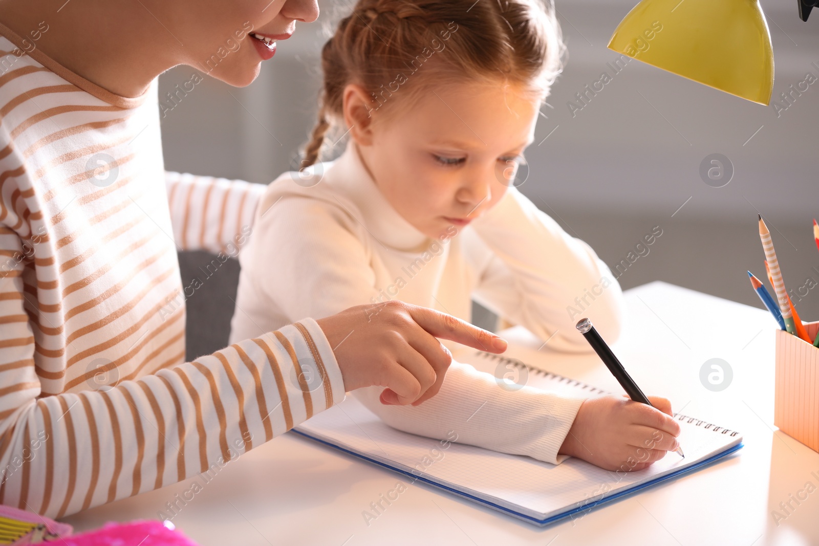 Photo of Woman helping her daughter with homework at table indoors