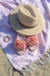 Photo of Blanket with stylish slippers and straw hat on sandy beach, above view
