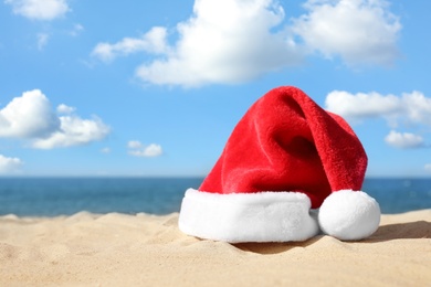 Photo of Santa's hat on sandy beach, space for text. Christmas vacation