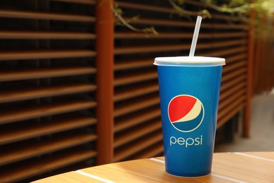 Photo of MYKOLAIV, UKRAINE - JUNE 9, 2021: Paper Pepsi cup on wooden table outdoors, space for text