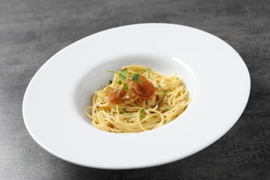 Photo of Tasty spaghetti with prosciutto and microgreens on grey table, closeup. Exquisite presentation of pasta dish