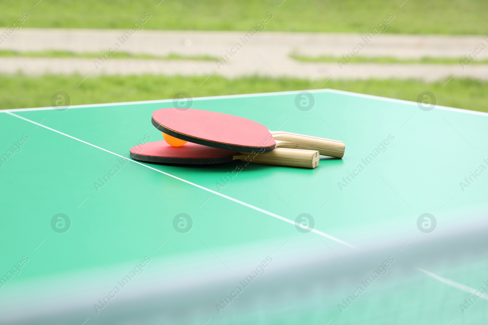 Photo of Tennis rackets and ball on ping pong table in park