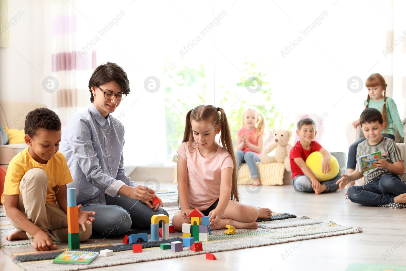 Photo of Young woman playing with little children indoors