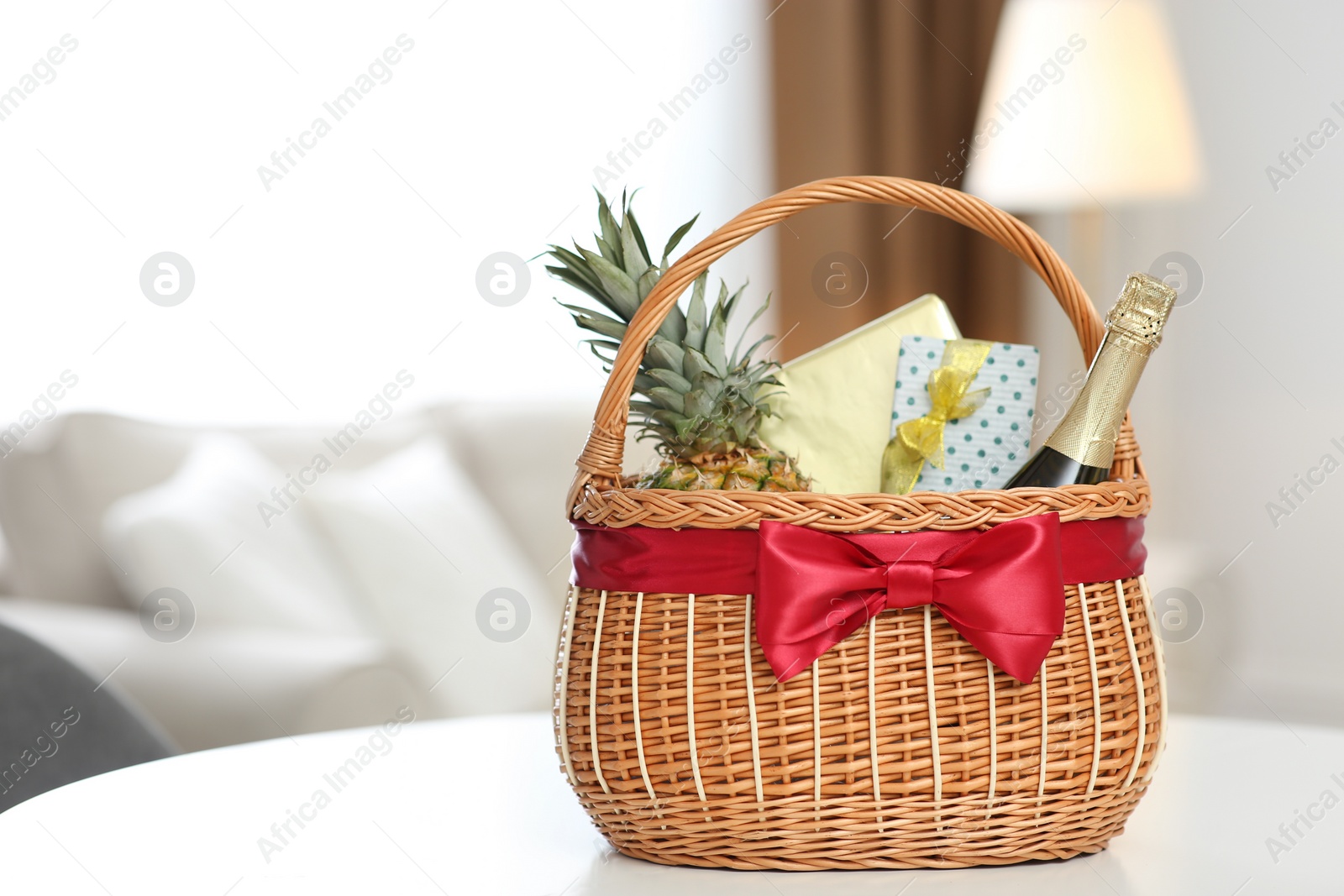 Photo of Wicker basket full of gifts on white table in living room. Space for text