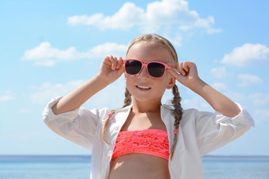 Little girl wearing sunglasses at beach on sunny day