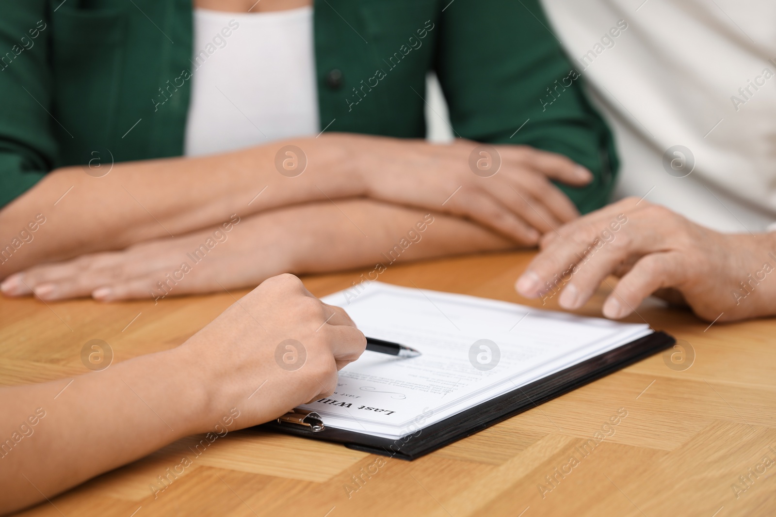 Photo of Notary showing senior couple where to sign Last Will and Testament at wooden table, closeup