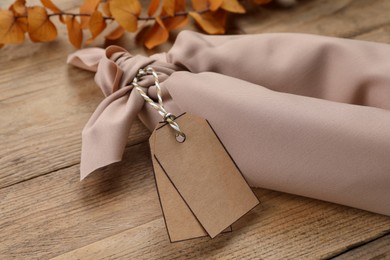 Photo of Furoshiki technique. Gift packed in beige fabric with tags on wooden table, closeup