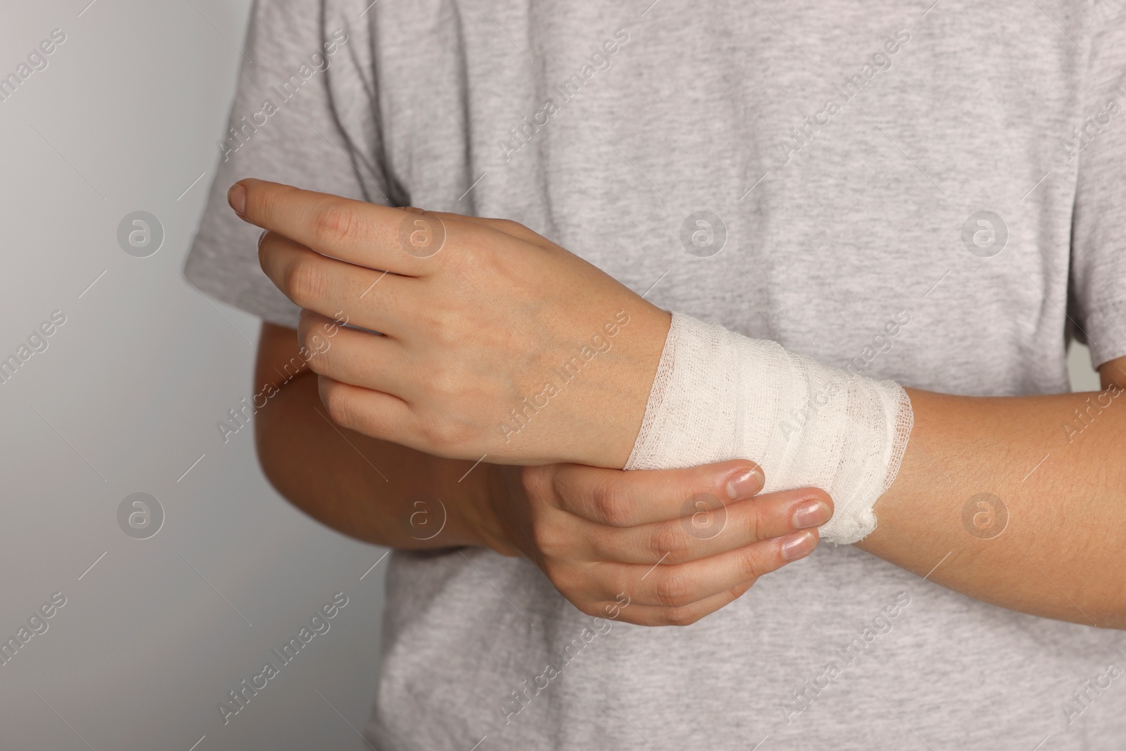 Photo of Woman with wrist wrapped in medical bandage on light grey background, closeup