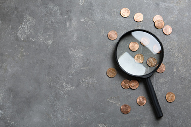 Photo of Magnifying glass and coins on grey stone table, flat lay with space for text. Search concept