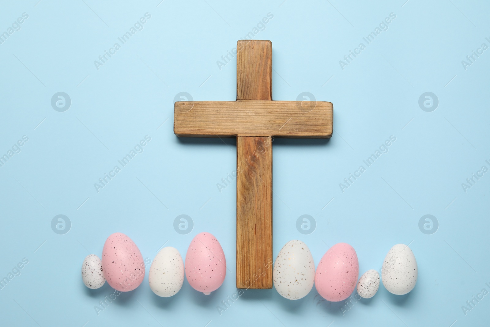 Photo of Wooden cross and painted Easter eggs on light blue background, flat lay