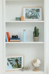 Photo of Beautiful pictures, potted cactus and different decorative elements on shelving unit