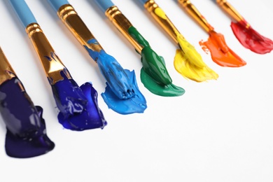 Photo of Set of brushes with different paints on white background, closeup. Rainbow colors