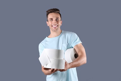 Photo of Young man holding toilet paper rolls on color background