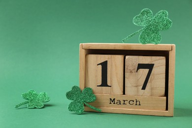 Photo of St. Patrick's day - 17th of March. Block calendar and decorative clover leaves on green background. Space for text