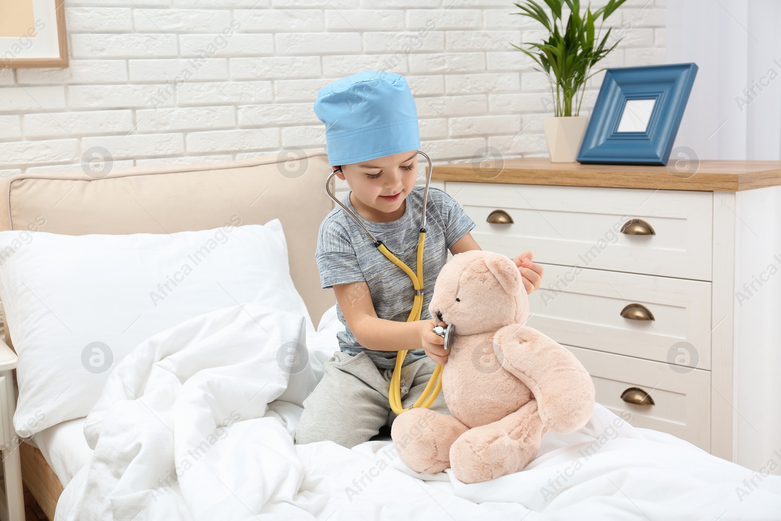 Photo of Cute child playing doctor with stuffed toy on bed in hospital ward