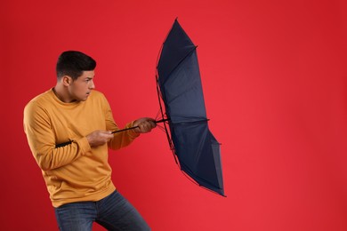 Emotional man with umbrella caught in gust of wind on red background