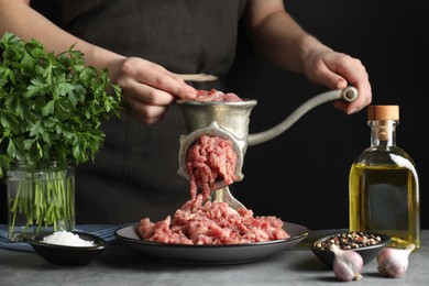 Photo of Woman making beef mince with manual meat grinder at grey table, closeup