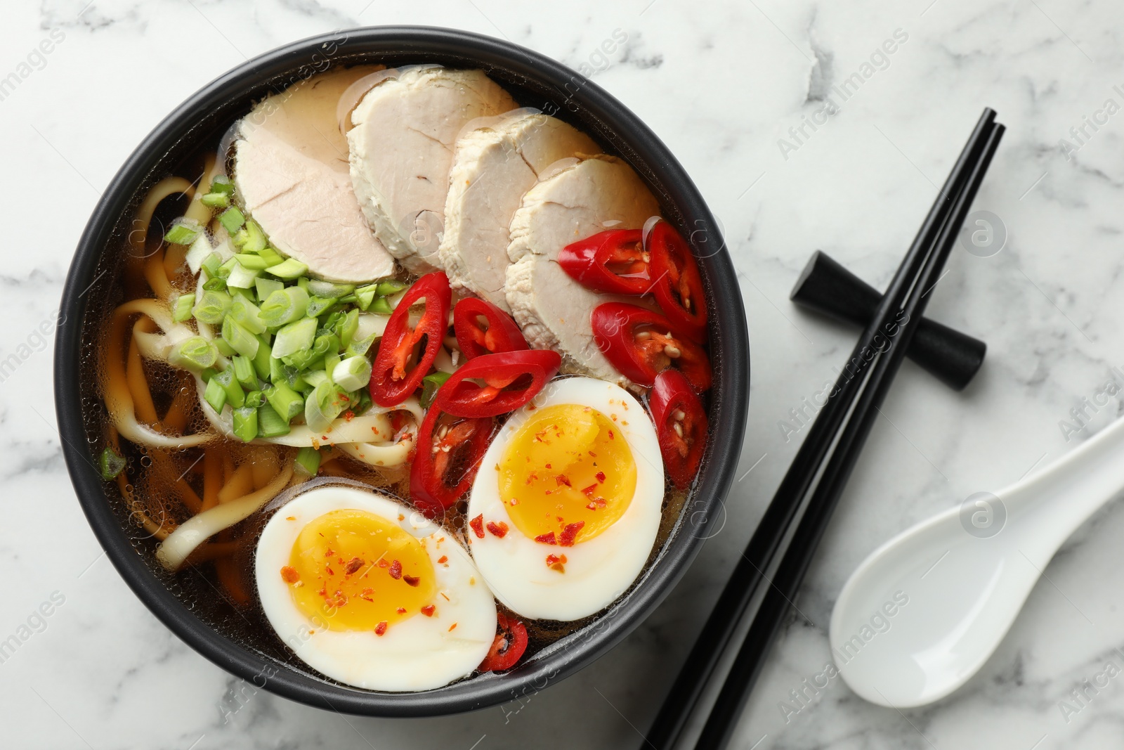 Photo of Delicious ramen in bowl and spoon on white marble table, flat lay. Noodle soup